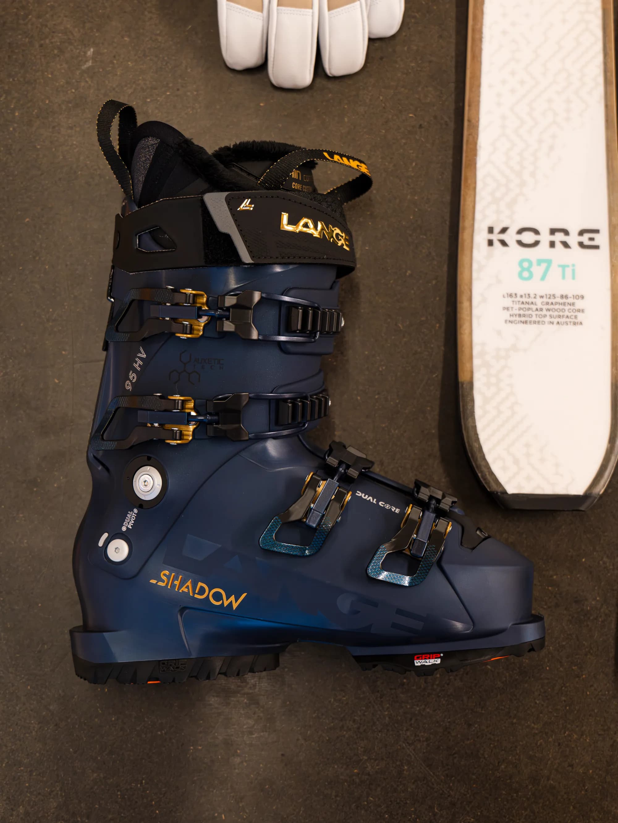 Chaussure de ski bleu marine aux détails dorés, posée à plat à côté d'un ski blanc